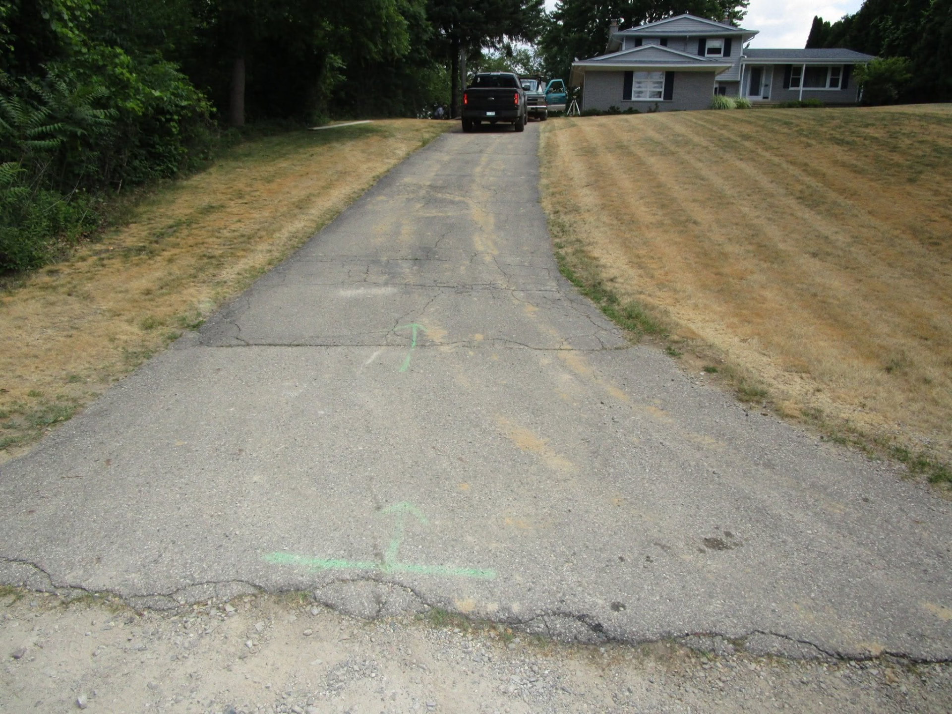 Before replacement: worn, cracked asphalt driveway climbing a hillside lot. Marcucci Concrete Construction in Oakland County, Michigan.