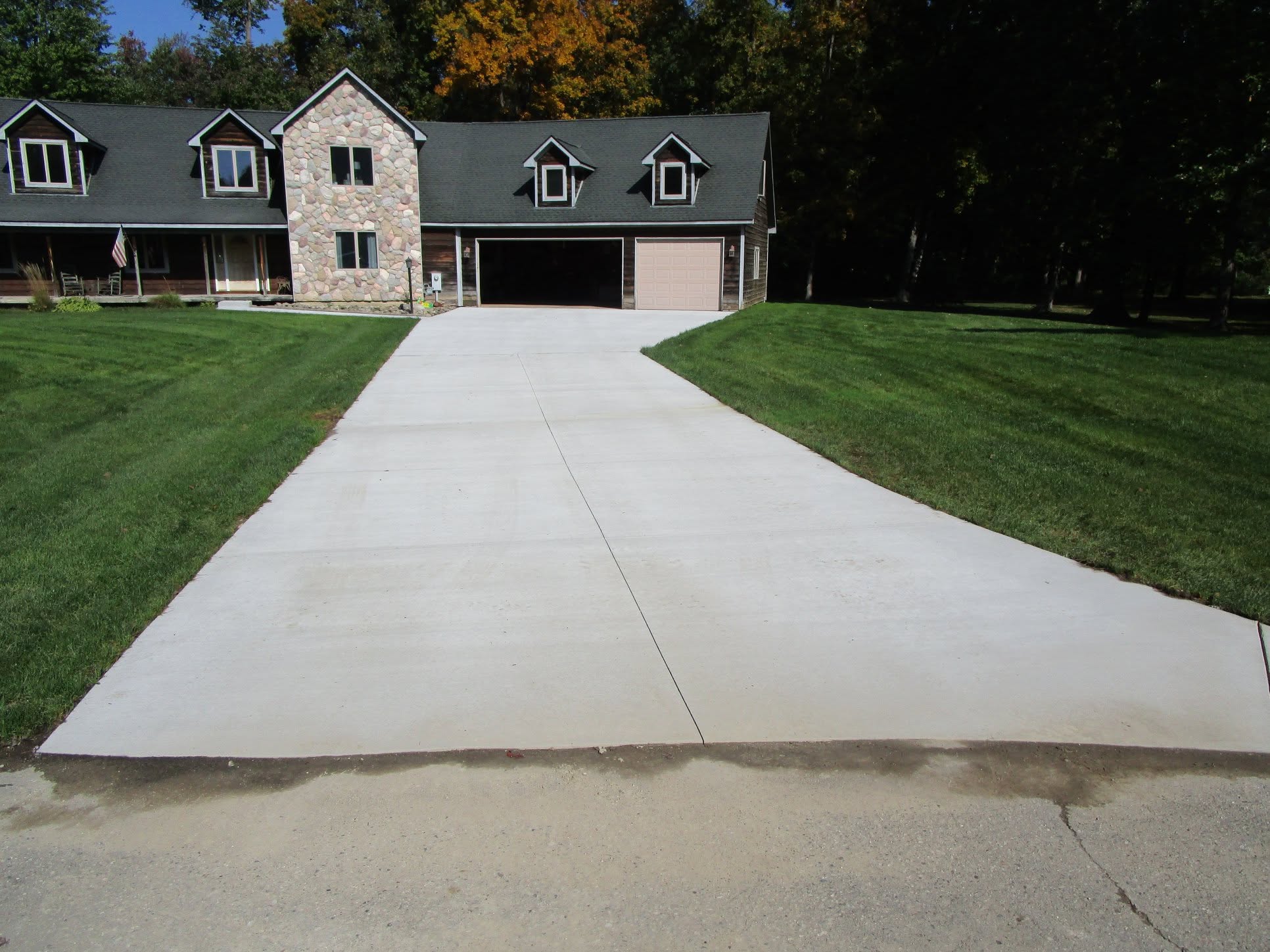 Wide concrete driveway replacement in front of a stone ranch home, completed by Marcucci & Son concrete driveway contractors after a full driveway tear-out in Oakland County, MI