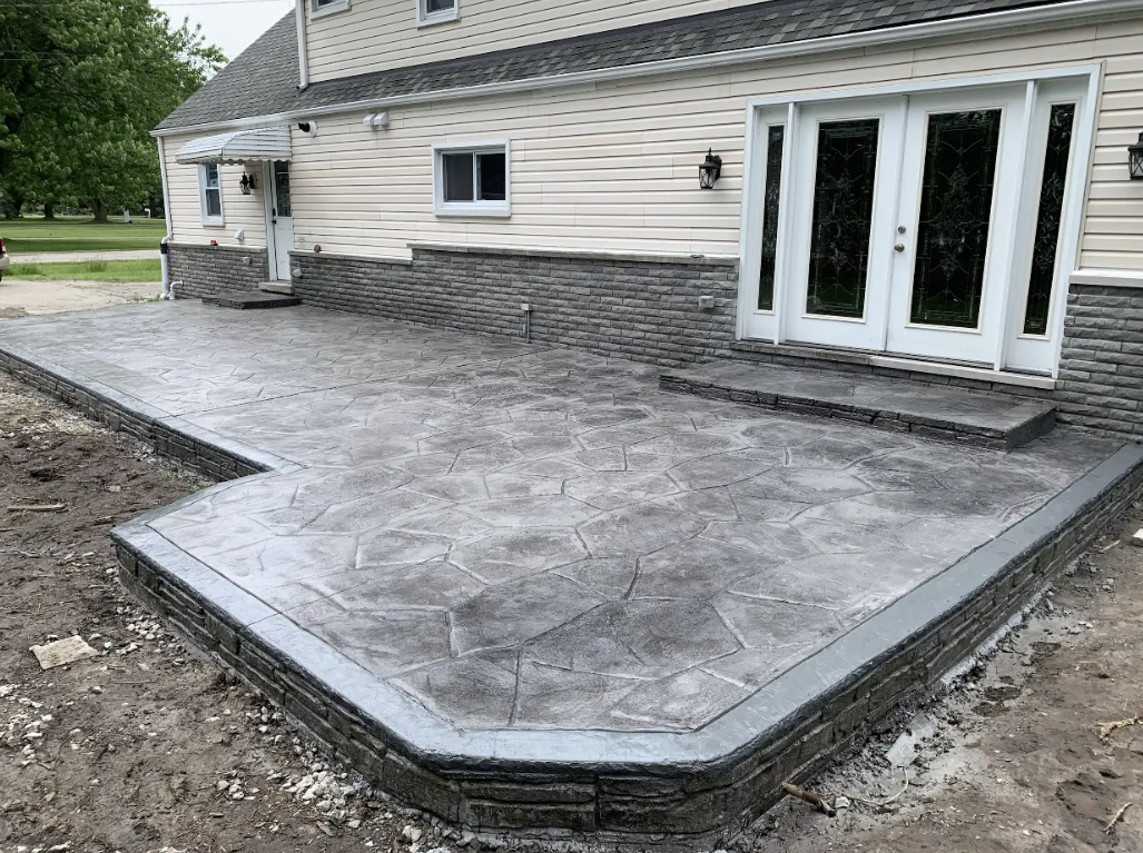 Gray stamped concrete patio with raised stone-texture border and matching step by Marcucci Concrete Construction in Oakland County, Michigan
