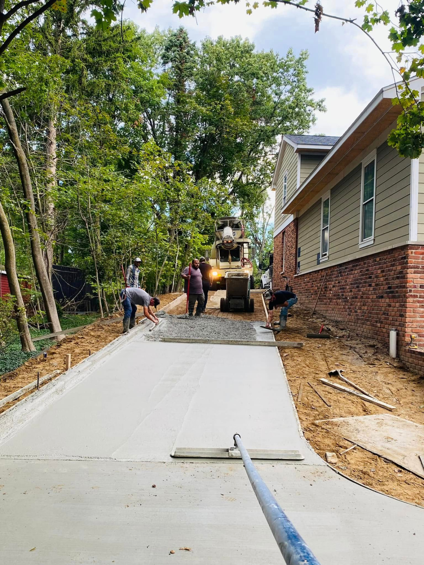 Marcucci crew placing and finishing a residential concrete driveway alongside a brick home using a ready-mix truck chute. Marcucci Concrete Construction in Oakland County, Michigan.