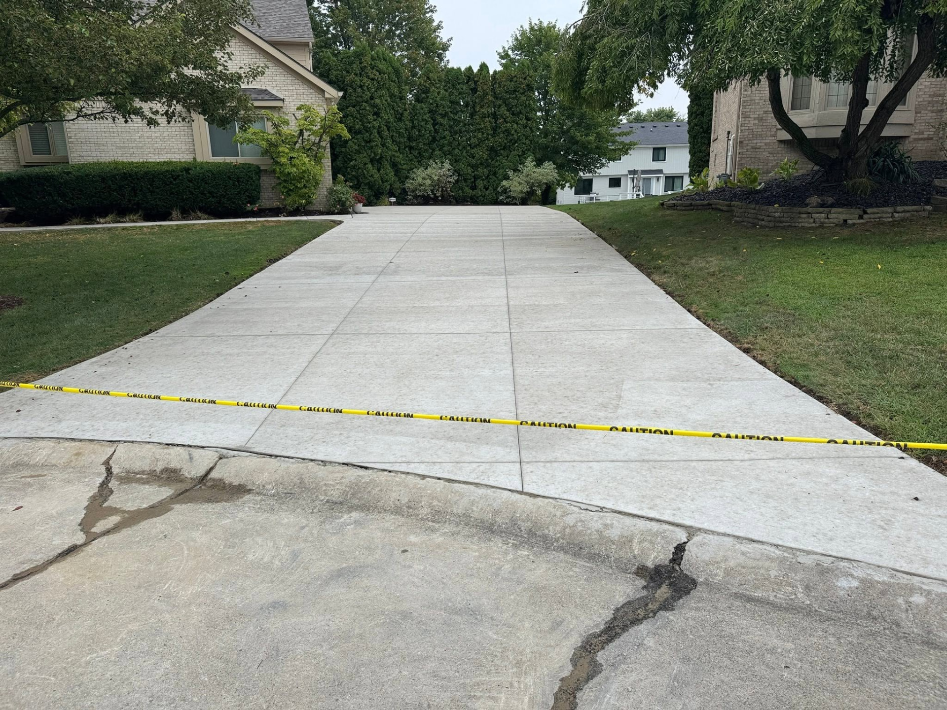 Finished broom-finish concrete driveway with control joints and caution tape at the street approach. Marcucci Concrete Construction in Oakland County, Michigan.