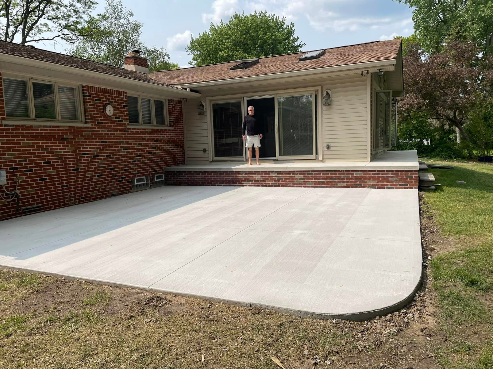 Large broom-finish backyard patio with a rounded corner and raised brick entry stoop. Marcucci Concrete Construction in Oakland County, Michigan.
