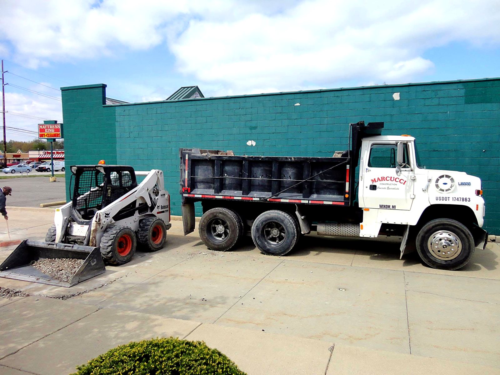 Marcucci Construction dump truck and Bobcat skid steer on a retail strip center sidewalk replacement
