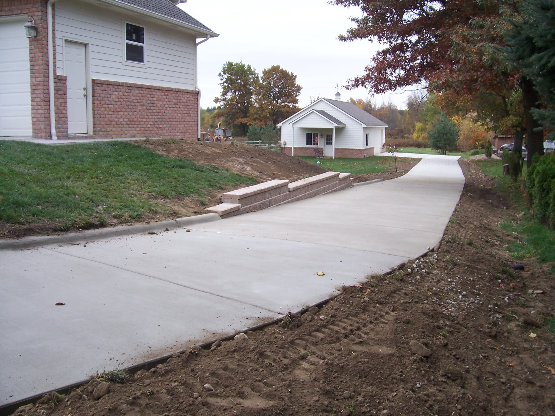 Long concrete driveway following a tiered retaining wall beside a home and outbuilding. Marcucci Concrete Construction in Oakland County, Michigan.