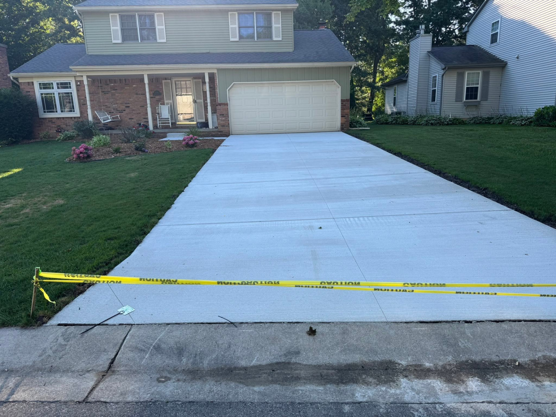 Fresh concrete driveway leading to a two-car garage at a colonial home, protected by caution tape. Marcucci Concrete Construction in Oakland County, Michigan.