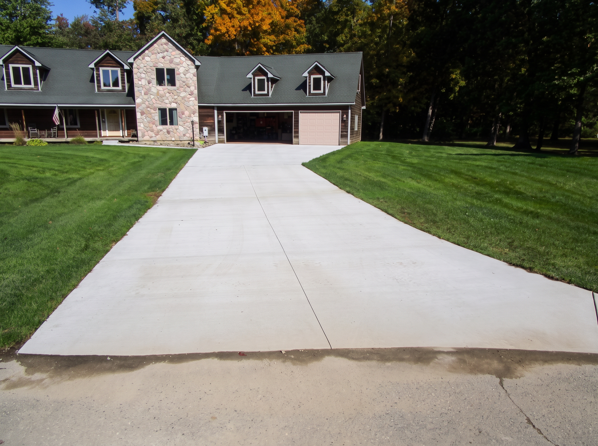Finished broom-finish concrete driveway with control joints at a stone-front home by Marcucci Concrete Construction